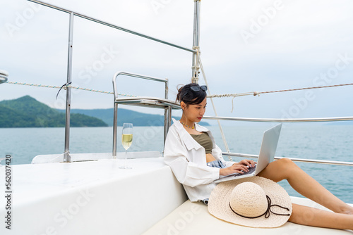 Attractive Asian woman enjoy outdoor lifestyle working on laptop computer while travel on luxury private catamaran boat yacht sailing in the ocean on summer holiday vacation at tropical island. © CandyRetriever 
