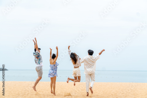 Group of Happy Asian people friends playing and jumping together on beach at seaside in sunny day. Man and woman enjoy and fun outdoor lifestyle travel at tropical island on summer holiday vacation.