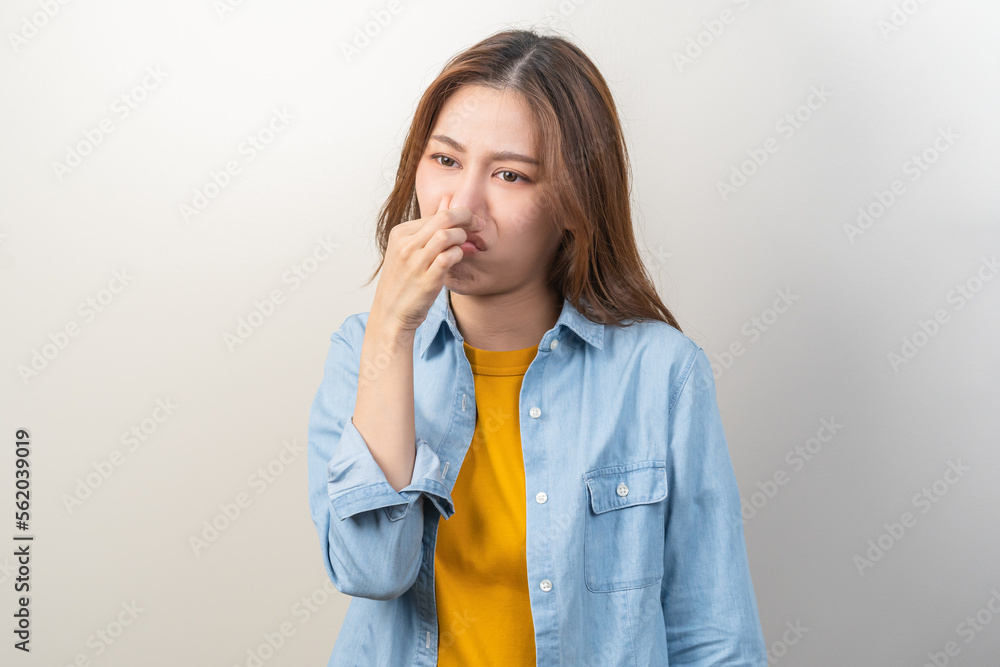 Portrait of pretty brunette hair, disgust smell bad strong asian young woman, girl hand squeezing, covering nose with fingers, expression face disgusting, dislike odor isolated on white background. Portrait of pretty brunette hair, disgust smell bad strong asian young woman, girl hand squeezing, covering nose with fingers, expression face disgusting, dislike odor isolated on white background.