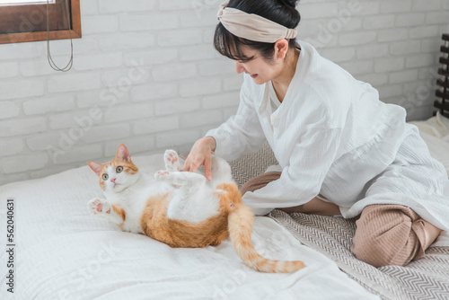 ベッドルームで猫・ペットと遊ぶ飼い主のアジア人女性（お腹・パジャマ）