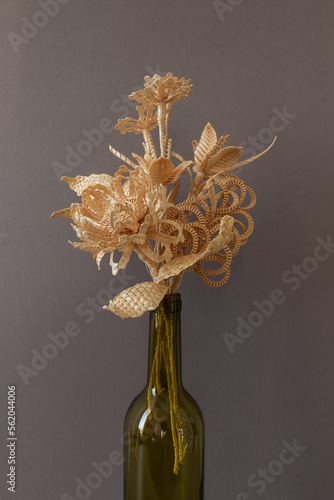 The flowers is made of straw on a gray background in an empty bottle