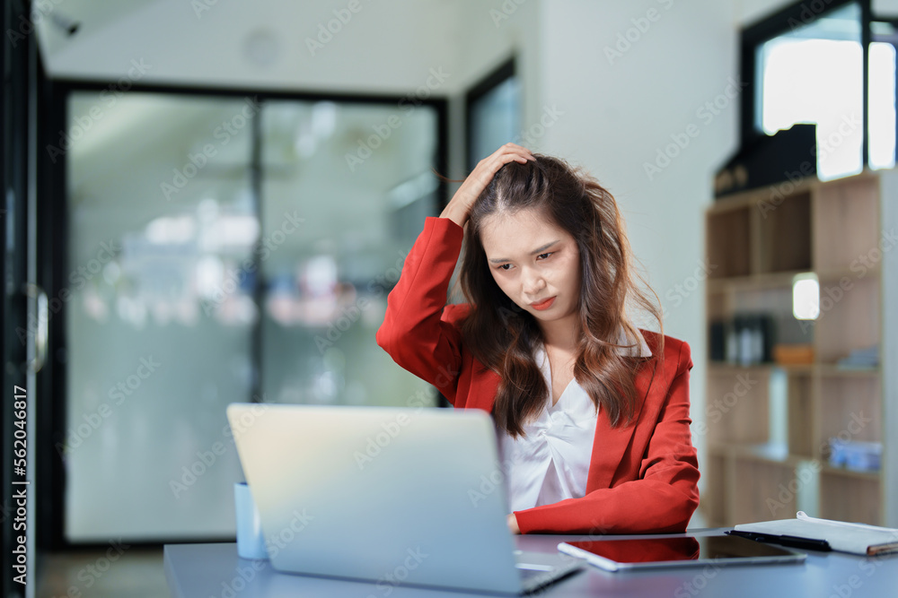 Portrait of a young Asian woman showing a serious face as she uses her phone, financial documents and computer laptop on her desk in the early morning hours Portrait of a young Asian woman showing a serious face as she uses her phone, financial documents and computer laptop on her desk in the early morning hours