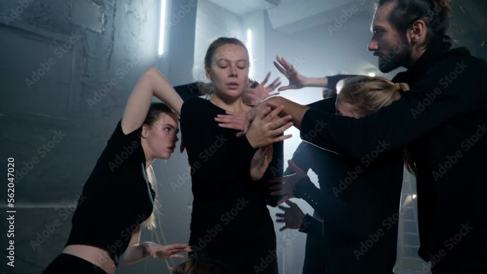 Theatrical troupe moving hands around body of young slim actress at backlit. Young talented Caucasian men and women rehearsing modern play on backstage indoors. Performance and art concept Theatrical troupe moving hands around body of young slim actress at backlit. Young talented Caucasian men and women rehearsing modern play on backstage indoors. Performance and art concept