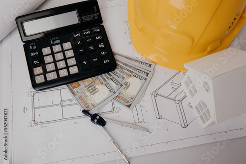 Construction drawings, safety hat, calculator and house model on a table