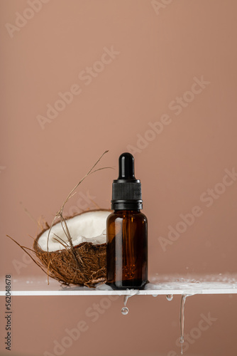 Glass-brown serum with a skin care pipette and coconut, with water drops on a beige background. Health and beauty concept