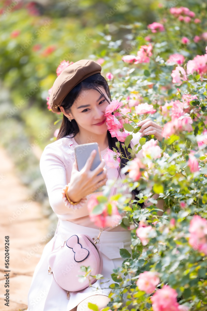 Fototapeta premium Beautiful woman holding a bouquet of roses and make selfie by smartphone in the garden. Happy woman smelling rose and taking selfie with smartphone. Valentine's day concept,Selfie of happy of smiling.