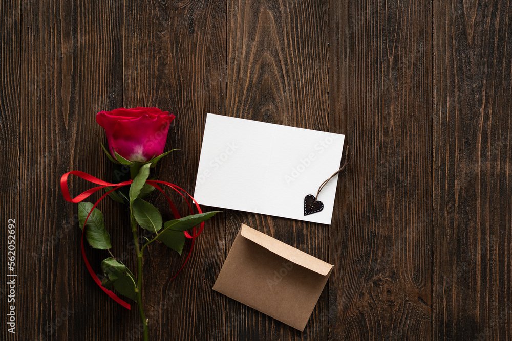 Red rose with postcard on wooden background. Happy Valentines Day postcard. Love concept for mothers day or valentines day. Valentine card with space for text Red rose with postcard on wooden background. Happy Valentines Day postcard. Love concept for mothers day or valentines day. Valentine card with space for text