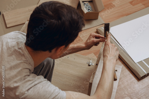 Tableau sur toile From above of man hammering wooden dowel while assembling new furniture in room