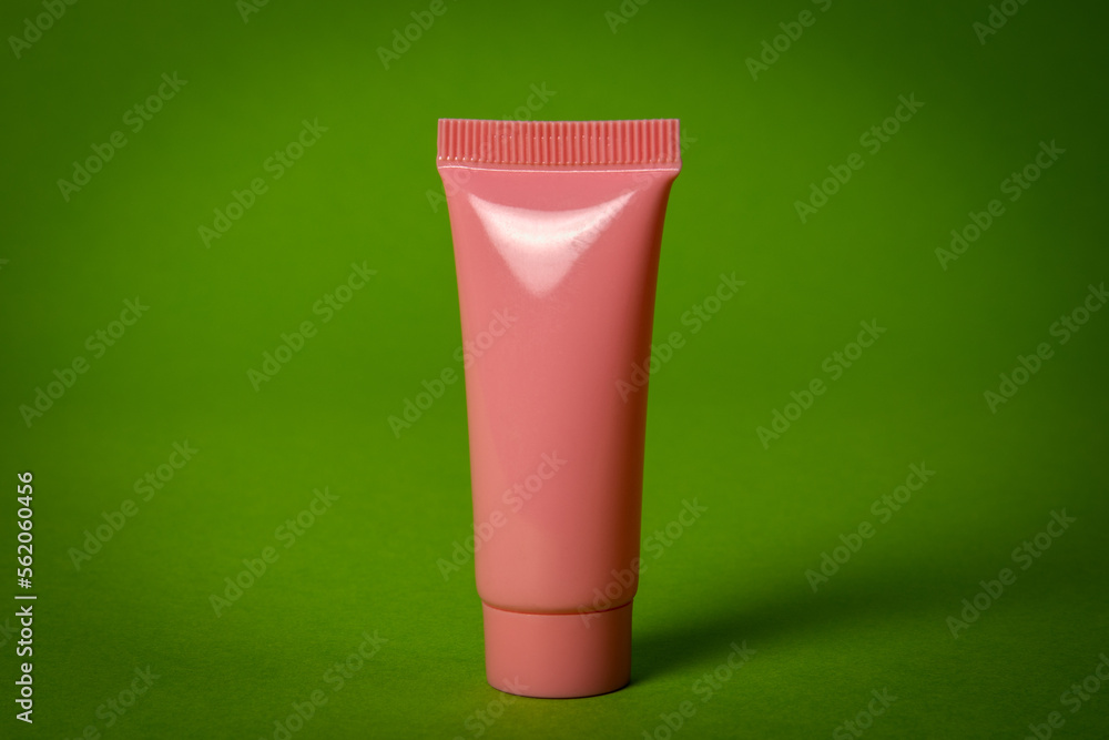Pink cosmetic tube on green background with copy space. Skin care, body treatment, beauty concept Pink cosmetic tube on green background with copy space. Skin care, body treatment, beauty concept