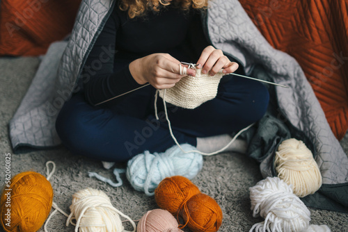 Close-up view of woman's hands knitting a scarf with patterns using needles, relaxing at home while doing favorite hobby activity. People lifestyle concept
