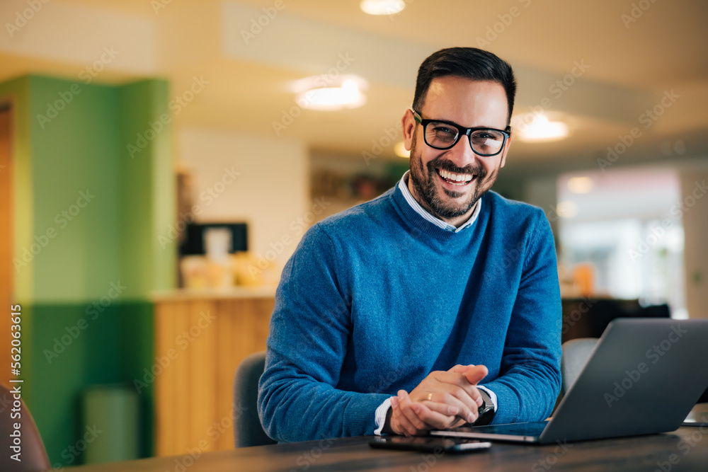 Portrait of a smiling male employee, using a laptop, sitting at the office. Portrait of a smiling male employee, using a laptop, sitting at the office.