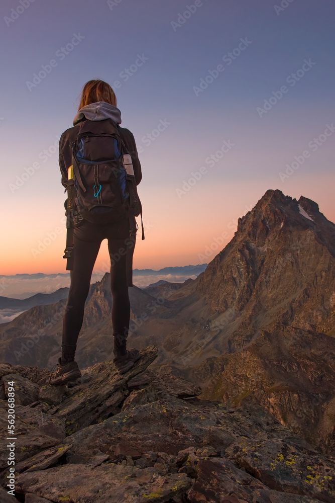 A young hiker posing admires a splendid colorful high altitude sunrise with Mount Viso (Monviso 3841 m) in the background on a beautiful summer morning. Italy, Piedmont, Monviso Natural Park.