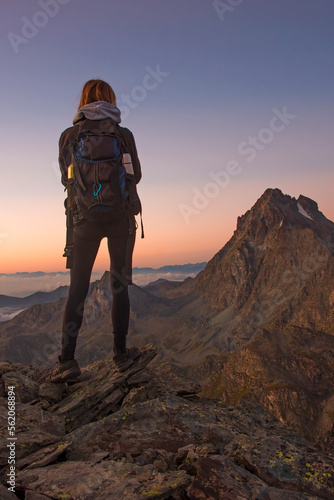 A young hiker posing admires a splendid colorful high altitude sunrise with Mount Viso (Monviso 3841 m) in the background on a beautiful summer morning. Italy, Piedmont, Monviso Natural Park.