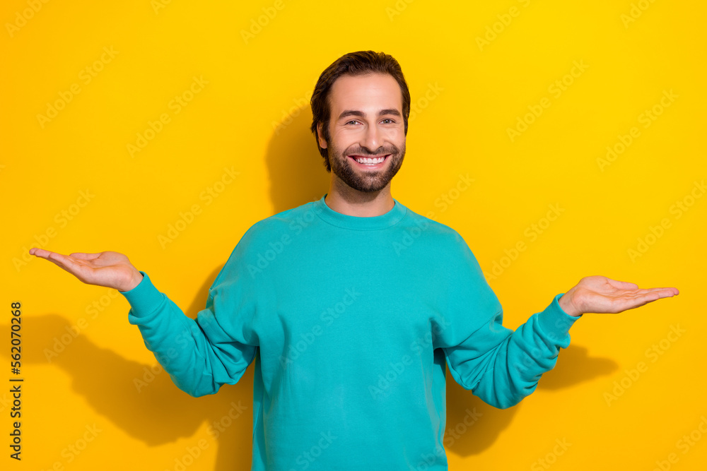 Photo of cheerful charming man wear turquoise clothes showing arms scales empty space isolated yellow color background Photo of cheerful charming man wear turquoise clothes showing arms scales empty space isolated yellow color background