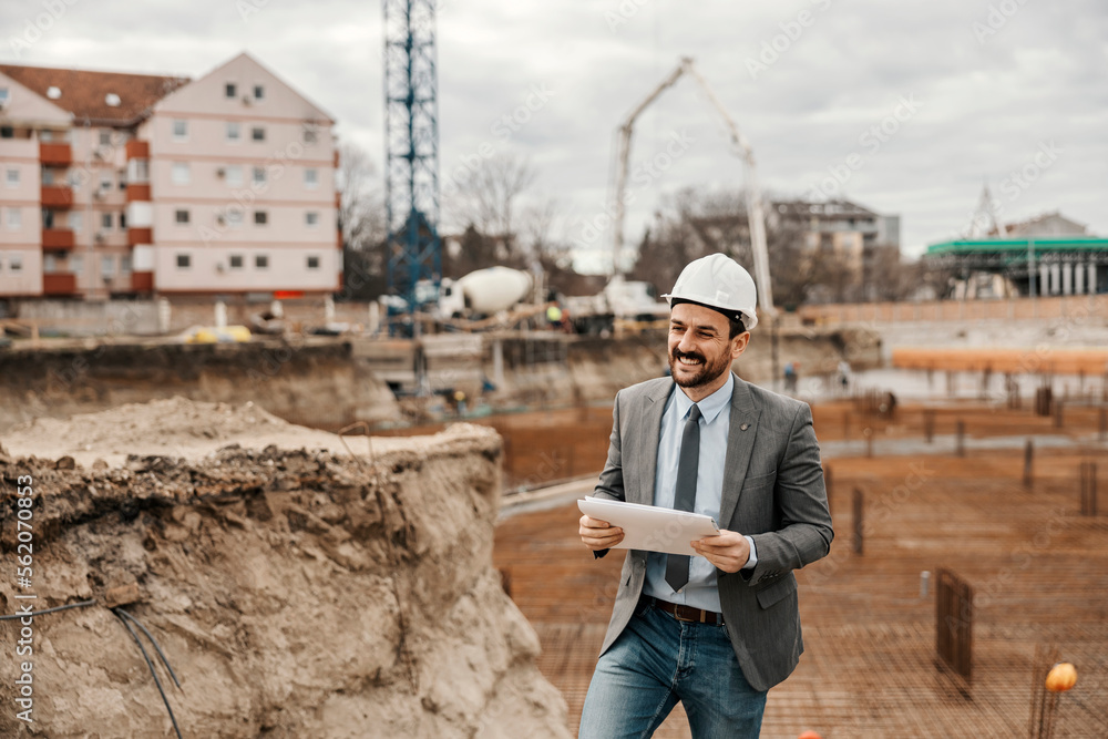 Fototapeta premium A happy contractor is standing on construction site with paperwork.