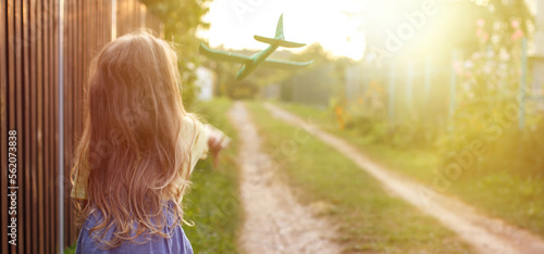 Print op canvas Happy child girl with long blond hair playing with toy airplane outdoor at sunse