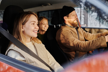 Happy family of three sitting in car and smiling, they travelling together during winter holidays