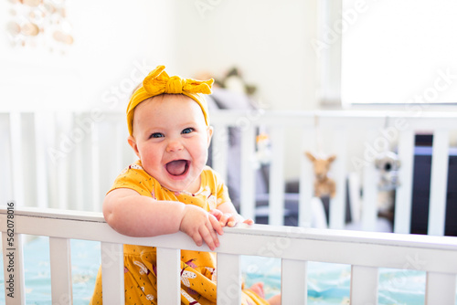Joyful happy baby sitting in cot in bedroom with copy space
