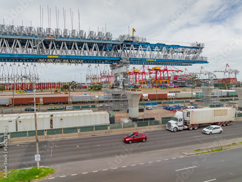 A large suspension crane building an elevated freeway next to a busy highway