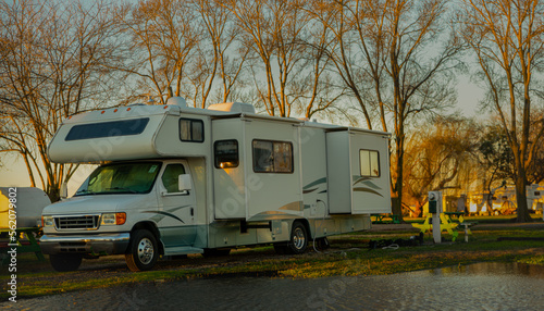 Rv class C motorhome with slides out parked camping next to water early morning light