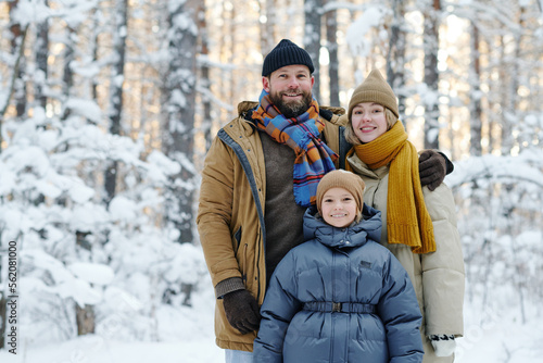 Portrait of happy family with their daughter smiling at camera together standing in winter forest