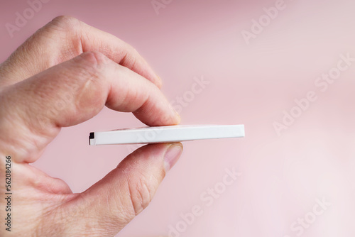 Swollen phone battery in a person's fingers on a pink background