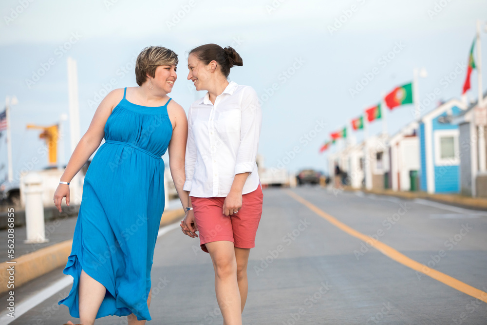 A same sex couple walks while looking at each other and smiling. A same sex couple walks while looking at each other and smiling.