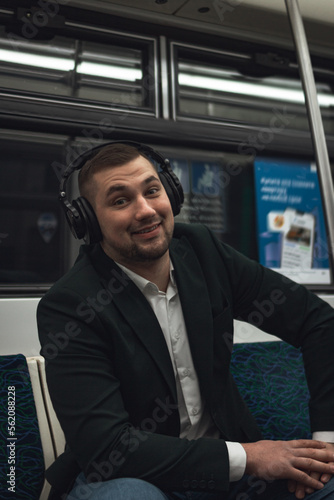 man young male caucasian passenger one person positively cheerful listens to music in headphones, smiles and go by subway transport in the morning. concept subscription to music. © evgris