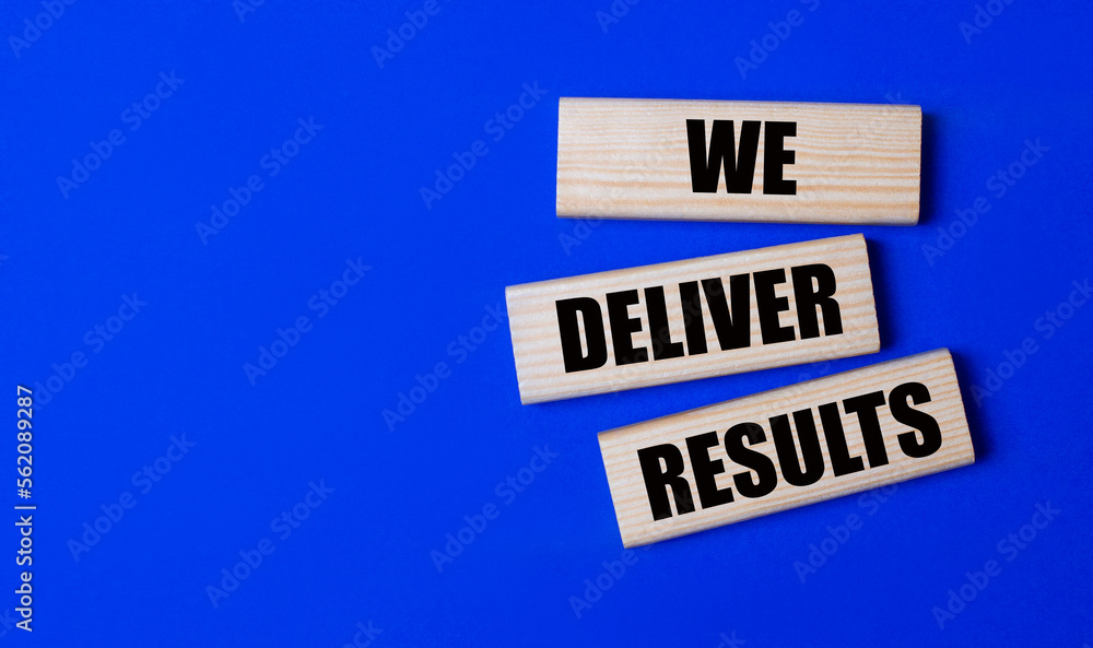 Three wooden blocks with the text WE DELIVER RESULTS on a bright blue background. Copy space