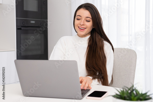 Cheerful woman laughs at online meeting with colleagues looking in Notebook. Young employee with long loose hair sits in chair smiling closeup slow motion © vladim_ka