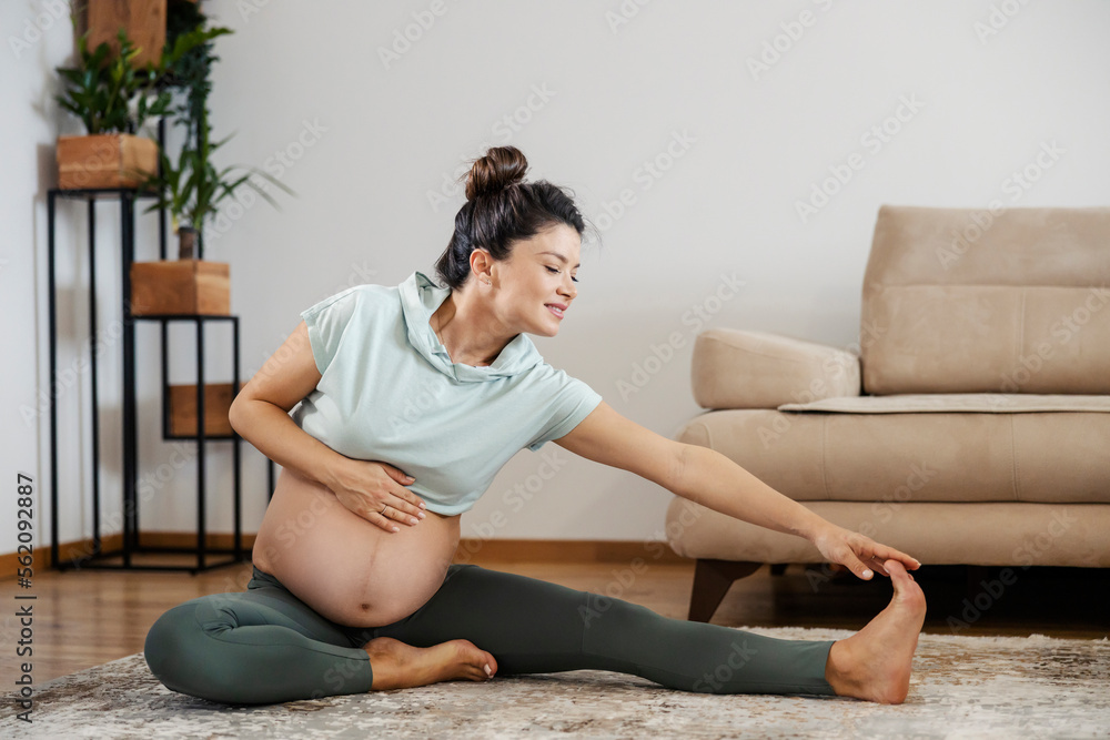 A fit pregnant woman is doing yoga exercises at home.