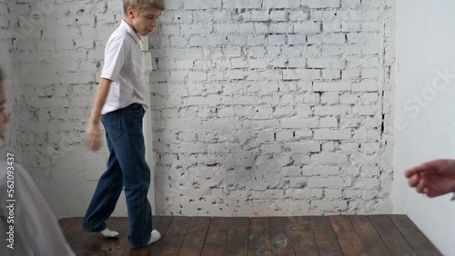 Teenage boy in white shirt does cartwheel on wooden stage in corner of photo studio at family gathering