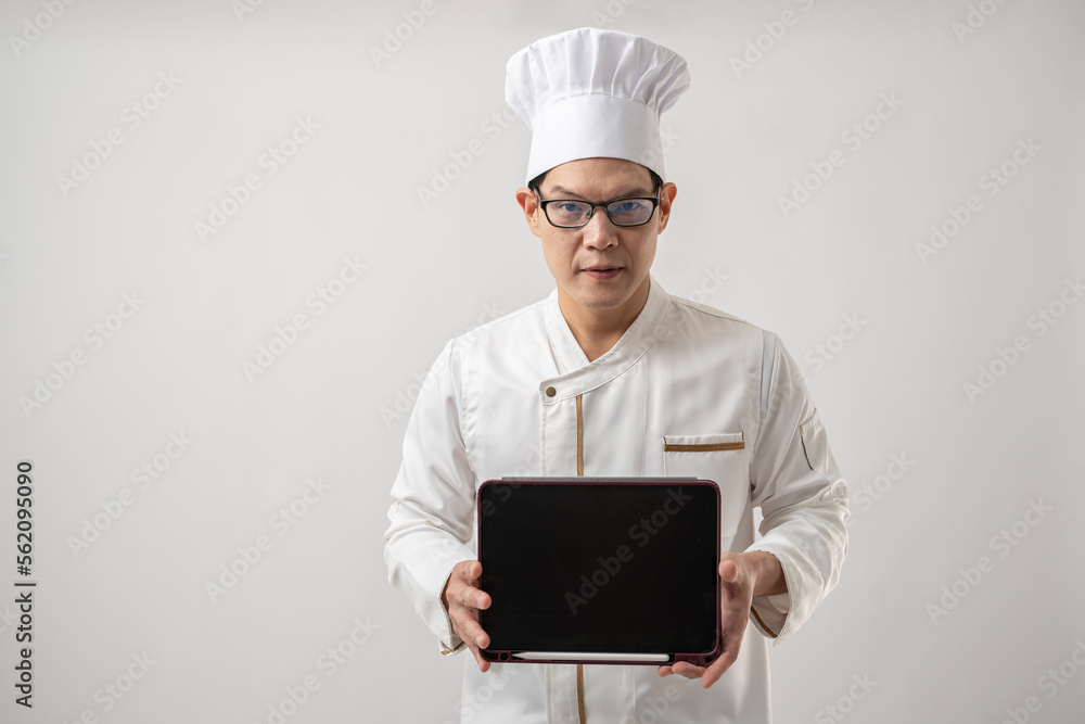 Portrait of confident Asian chef in uniform showing tablet blank black screen isolated on white background Portrait of confident Asian chef in uniform showing tablet blank black screen isolated on white background