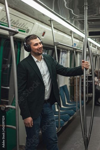 man young male caucasian passenger one person stands positively cheerful listens to music in headphones, smiles and go by subway transport in the morning. concept subscription to music.