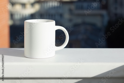 A white mug on the windowsill with a view of the city