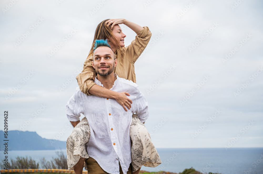 A young couple walks on a road surrounded by nature, with the man carrying the woman on his back A young couple walks on a road surrounded by nature, with the man carrying the woman on his back