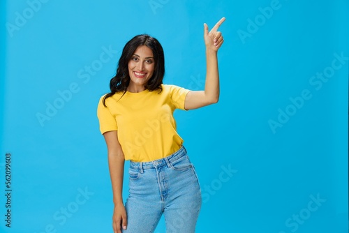 Woman in yellow t-shirt on blue background posing gestures emotions and signals with smile, hands up happiness copy space