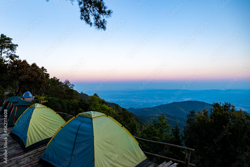 View of tents camping at the campsite in the woods with mountain range background. View of tents with mountain and beautiful sky background. Nature tourisium  and tents camping concept.