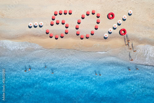 Creative text - 50% made from colorful umbrellas on sandy beach and blue sea with waves at sunny day. Aerial view of sea coast and text. Summer sale and discount. Background. Top view of clear water