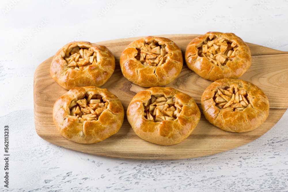 Sweet mini pies with apples and cinnamon on a wooden board with a napkin on a light gray background, close up. Delicious homemade food
