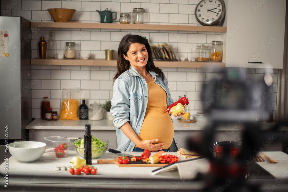 Beautiful pregnant woman filming cooking vlog. Happy woman filming her blog about healthy food at home..