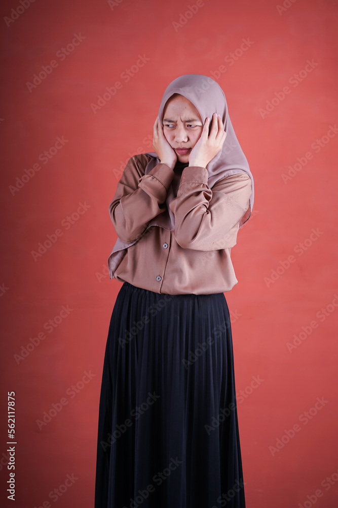 Beautiful Asian woman in brown shirt and headscarf covering ears with hands on brown background Beautiful Asian woman in brown shirt and headscarf covering ears with hands on brown background