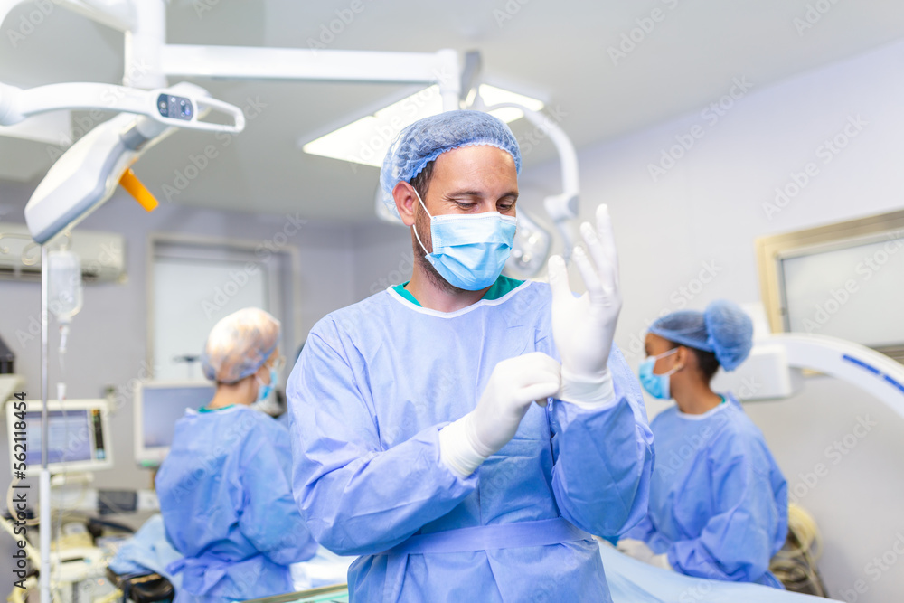 Portrait of male doctor surgeon putting on medical gloves standing in operation room. Surgeon at modern operating room Portrait of male doctor surgeon putting on medical gloves standing in operation room. Surgeon at modern operating room