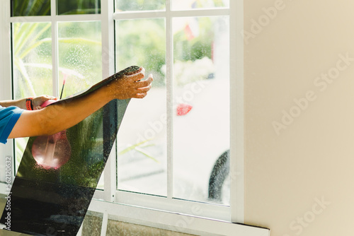 Woker wrapping tinting a house window with tinted foil using foggy spray.