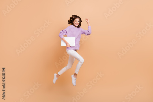 Full size photo of pretty adorable woman with curly hairdo wear knit sweater hold laptop hurry work isolated on beige color background