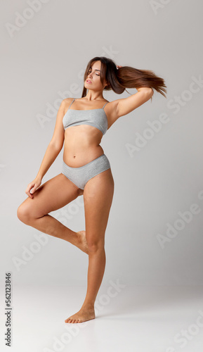 Comfort. Portrait of young beautiful girl with slim body posing in cotton underwear over grey studio background. Concept of body and skin care, fitness