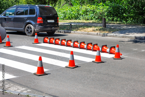 Pedestrian marking across the asphalt road on a summer day is fenced with traffic cones.