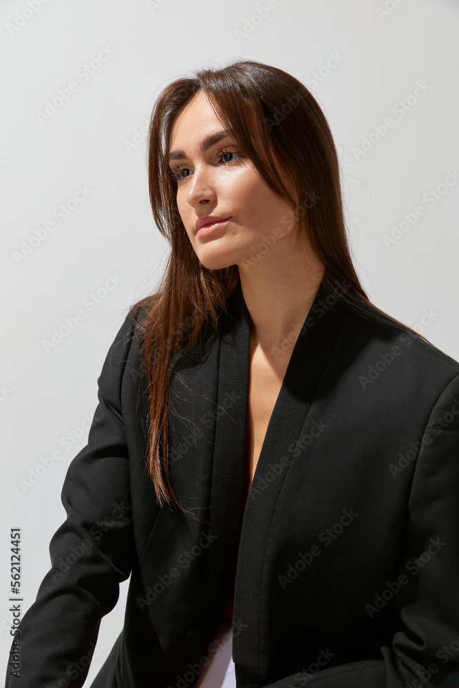 Portrait of young beautiful girl posing in black classic suit over grey studio background. Concept of body and skin care, fitness Portrait of young beautiful girl posing in black classic suit over grey studio background. Concept of body and skin care, fitness