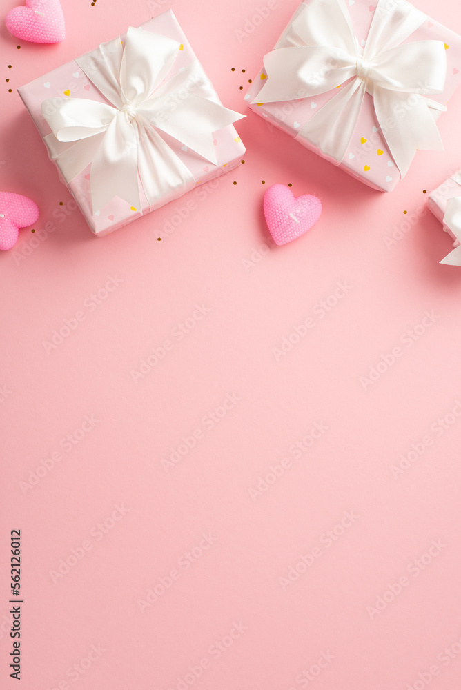 Valentine's Day concept. Top view vertical photo of gift boxes with white ribbon bows heart shaped candles and golden confetti on isolated pastel pink background with empty space