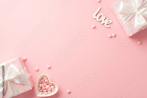 St Valentine's Day concept. Top view photo of present boxes with silk ribbon bows heart shaped saucer with sprinkles and inscription love on isolated pastel pink background with blank space
